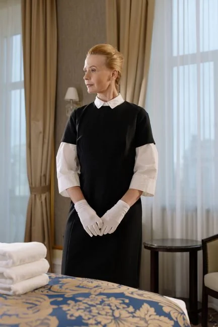 A housekeeper elegantly arranges bed sheets in a luxurious hotel room, showcasing hospitality expertise.